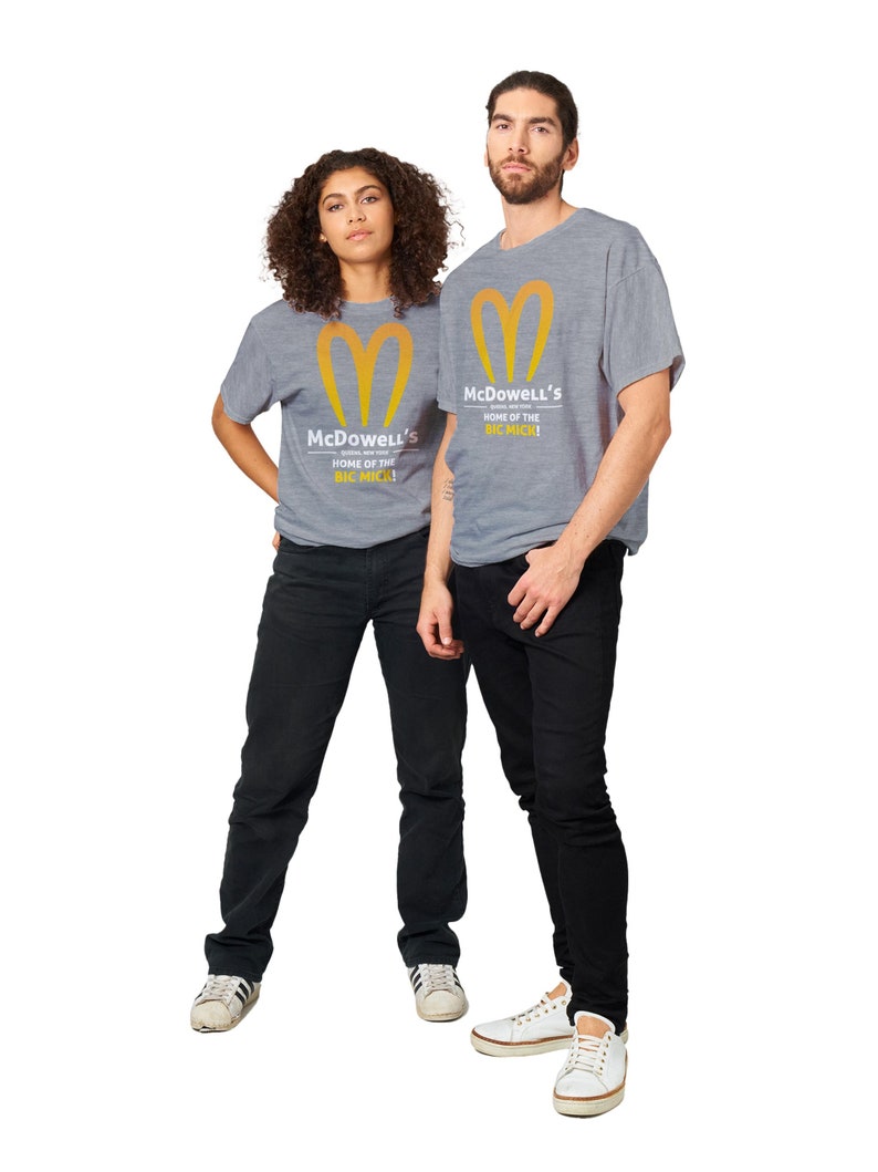 May include: Two people wearing gray t-shirts with the McDowell's logo and text. The logo is a stylized yellow heart shape. The text reads "McDowell's HOME OF THE BIC MICK!". They are wearing black pants and white sneakers.