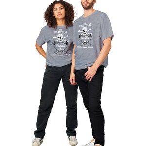 May include: Two people wearing grey t-shirts with a white skull and crossbones graphic. The graphic says "The Fratellis Lighthouse Lounge Astoria Oregon".