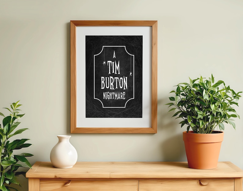 K&ouml;nnte beinhalten: Ein gerahmter Druck mit dem Text "A Tim Burton Nightmare" in Wei&szlig; auf schwarzem Hintergrund. Der Druck befindet sich in einem Holzrahmen und wird auf einem Holztisch mit einer wei&szlig;en Vase und einer Topfpflanze ausgestellt.