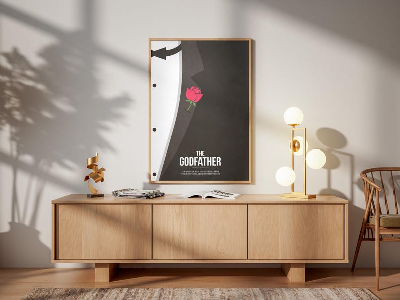 May include: Framed poster featuring a minimalist design from "The Godfather" movie. The artwork shows a black suit with a white shirt and a red rose. The title "THE GODFATHER" is displayed in white text.