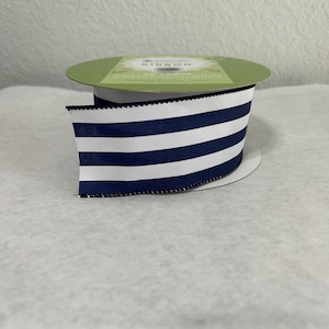 May include: A roll of navy blue and white striped ribbon. The ribbon has a scalloped edge and is on a green cardboard spool. The ribbon is likely used for crafts, gift wrapping, or decorations.