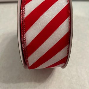 Könnte beinhalten: Eine Rolle rot-weiß gestreiftes Band. Das Band hat diagonale Streifen in Rot und Weiß mit einer glitzernden Textur. Die Kanten sind mit einem rot genähten Rand versehen. Dieses dekorative Band eignet sich für Bastelarbeiten und Geschenkverpackungen.
