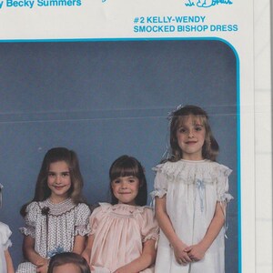May include: Five young girls wearing smocked bishop dresses in various colors, including white, pink, blue, and a white dress with black polka dots. The girls are standing and sitting in front of a blue background. The image includes the text "Briar Patch Designs, Inc. By Becky Summers #2 Kelly-Wendy Smocked Bishop Dress".