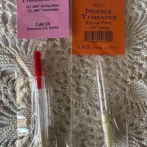 May include: Two needle threaders packaged in clear plastic bags. The threader on the left is red and white and labeled "MO15 Needle Threader Set (1) .004" Extra Fine (1) .006" Standard LACIS Berkeley, CA 94703". The threader on the right is white and labeled "MO13 Needle Threader Extra Fine .04" Wire 8 24649 00720 2 LACIS, Berkeley, CA 94703".