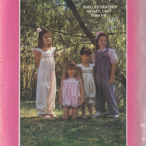May include: A pink and white sewing pattern cover featuring four young girls in various dresses and overalls. The text reads "SHELLEY, HEATHER, HAYLEY, LACY, Sizes 1-8" and "Yvonne Denise Designs". The background is a green, natural setting.