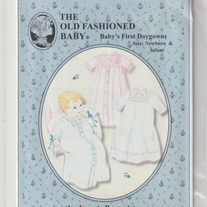 以下が含まれることがあります： Jeannie Baumeisterによる「The Old Fashioned Baby Baby's First Daygowns」というタイトルの裁縫型紙封筒。水色のカバーには、白いベビードレスを着た赤ちゃんのイラストと、ピンクのアクセントが入った2着の白いベビードレスのイラストが描かれています。