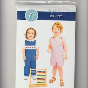 May include: A sewing pattern package featuring two children's outfits. One child wears a blue jumpsuit with a white collared shirt, the other a pink gingham romper. The package is labeled "JOHNNY" and indicates sizes for 3 to 12 months.