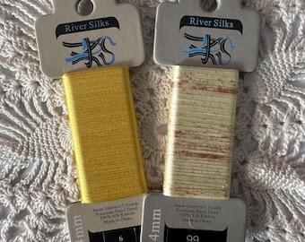 May include: Two spools of 4mm wide, 5.5 yard, hand-dyed silk ribbon. One spool is yellow and the other is a light beige with a subtle shimmer. Both spools have the text "River Silks" and "4mm-5meters/5.5yards Premium Hand Dyed 100% Silk Ribbon Made in China" printed on the label.