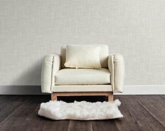 May include: A white armchair with a white cushion sits on a wooden floor with a white fluffy rug in front of it. The armchair has a light wood frame and a textured fabric upholstery.