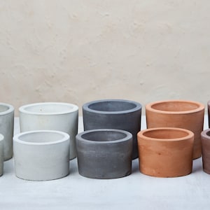 Pode incluir: Oito vasos de cimento em vários tons de cinza, marrom e branco. Os vasos estão dispostos em duas fileiras de quatro, com os vasos menores na frente.