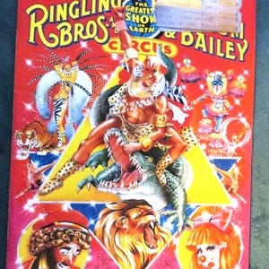 May include: A vintage circus poster featuring a colorful illustration of a lion, a crocodile, and a clown. The poster is red with yellow and white lettering that reads "Ringling Bros. and Barnum & Bailey Circus".