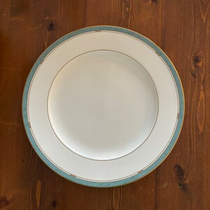 May include: A white ceramic dinner plate with a blue and gold rim. The plate has a simple design and is perfect for everyday use.