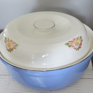 May include: A blue and white enamelware casserole dish with a lid. The lid has a floral design with pink and yellow flowers. The dish is perfect for serving a large meal.
