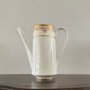 May include: White porcelain teapot with a gold trim and a delicate floral design. The teapot has a spout and a handle.