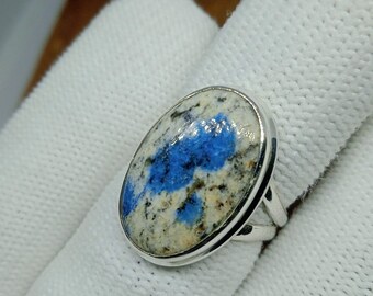 May include: Silver ring with an oval k2 stone. The stone has a distinctive blue and white pattern. The ring is shown on a white background. The ring is a piece of jewellery.