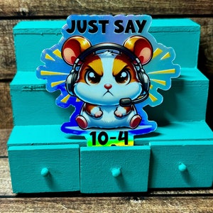 Pode incluir: Um adesivo hologr&aacute;fico com um hamster de desenho animado usando um fone de ouvido e dizendo "Just Say 10-4".