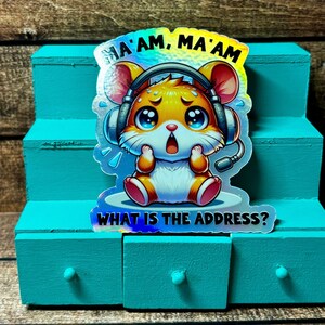 Pode incluir: Um adesivo hologr&aacute;fico com um hamster de desenho animado usando fones de ouvido e uma express&atilde;o de p&acirc;nico. O texto "Ma'am, Ma'am What is the address?" est&aacute; impresso no adesivo.