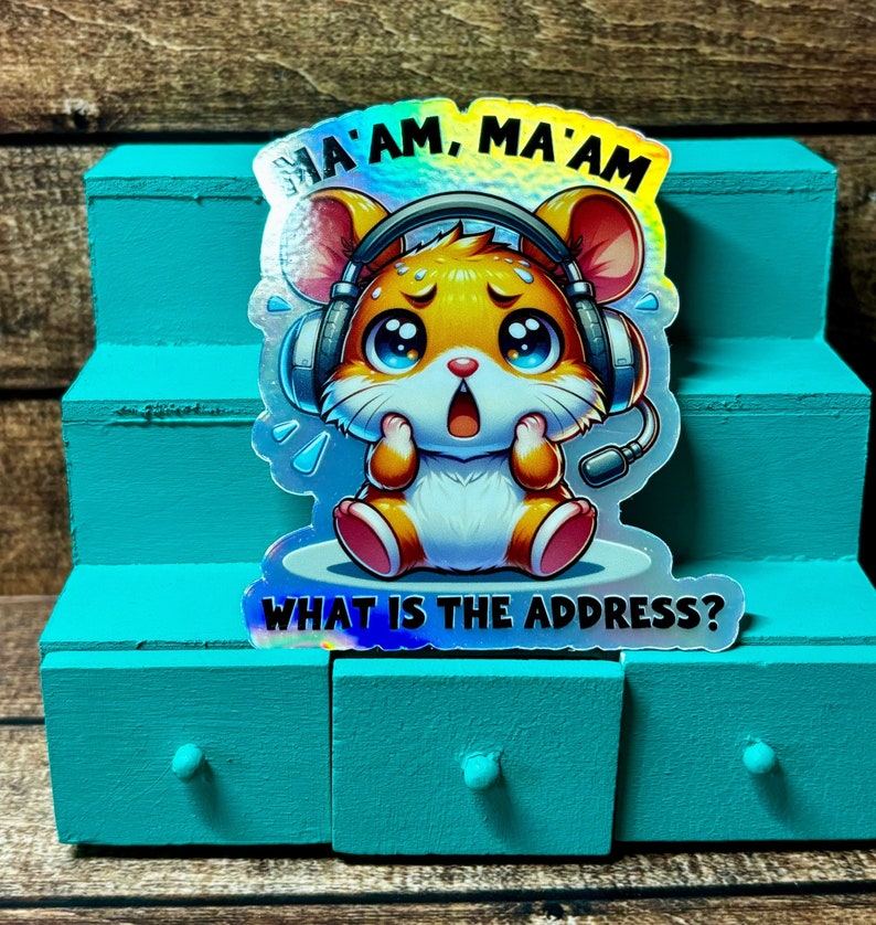 Pode incluir: Um adesivo hologr&aacute;fico com um hamster de desenho animado usando fones de ouvido e uma express&atilde;o de p&acirc;nico. O texto "Ma'am, Ma'am What is the address?" est&aacute; impresso no adesivo.