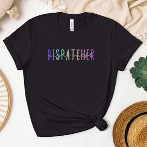 May include: Black t-shirt with a rainbow-colored graphic that says "DISPATCHER night shift".