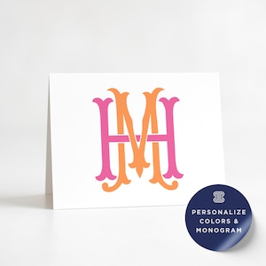 May include: A white card featuring a pink and orange monogram design. The monogram consists of the letters H and M, intertwined with decorative flourishes. A navy blue sticker with white text that says "PERSONALIZE COLORS & MONOGRAM" is in the bottom right corner.