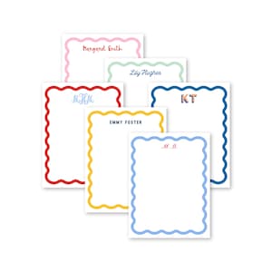 May include: A collection of personalized stationery notepads with scalloped edges. Each notepad features a different color border, including pink, red, yellow, blue, and green. The notepads are labeled with names or initials in various fonts.