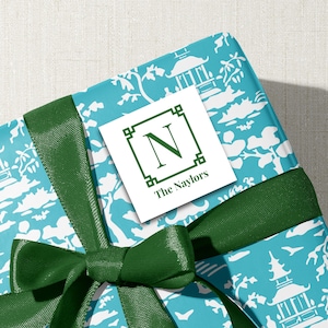 May include: A wrapped gift with turquoise and white patterned paper, tied with a dark green ribbon and bow. A white tag with a green border displays the letter "N" and the name "The Naylors".