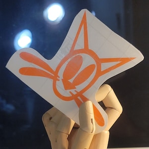 May include: Orange and white sticker with a cartoon bunny rabbit design. The bunny has large ears and a wide smile.