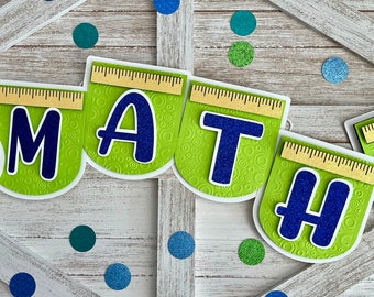Puede incluir: Una pancarta verde y azul con la palabra "MATH" en ella. Cada letra está en una hoja separada con una regla y símbolos matemáticos.