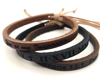 Puede incluir: Tres pulseras de cuero con diferentes mensajes grabados. La pulsera superior es marrón y dice "You're my Inspiration". La pulsera del medio es negra y dice "II.XVII.MM". La pulsera inferior es marrón y dice "Colossians 13:1 Ps".