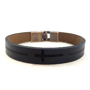 May include: Black leather bracelet with a cross design and a brass clasp.