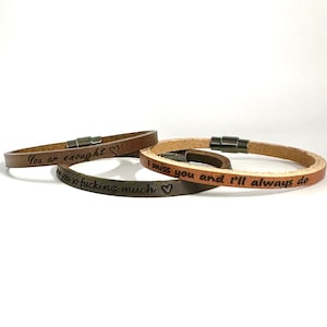 Peut inclure: Trois bracelets en cuir avec des messages gravés. Le bracelet du haut indique "You are enough" avec un symbole de cœur. Le bracelet du milieu indique "I miss you and I'll always do" et le bracelet du bas indique "Love you so fucking much" avec un symbole de cœur.