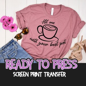 May include: Ready to press screen print transfer with a pink t-shirt featuring a black and white graphic of a coffee cup with the text "Hit me with your best pot".