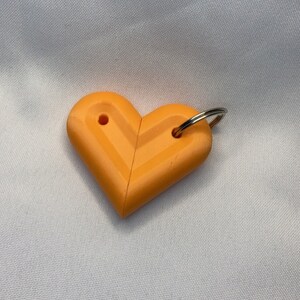 May include: A bright orange heart-shaped keychain with a silver metal ring. The heart is made of two interlocking pieces.