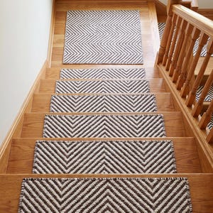 Peut inclure: Un ensemble de tapis d'escalier rectangulaires avec un motif chevron marron foncé et crème. Chaque tapis est posé sur une marche en bois, couvrant la partie centrale de l'escalier pour offrir une surface texturée sur le bois.
