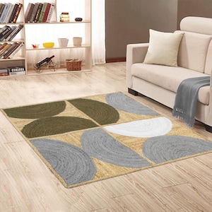 May include: A rectangular area rug with a geometric design. The rug features a natural beige background with semi-circular patterns in olive green, gray, and white. The rug is placed on a hardwood floor in a living room setting.