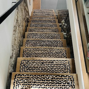 May include: A staircase featuring wooden steps adorned with rectangular stair treads in black and tan. The woven treads are placed on each step. The staircase is next to a stone wall.