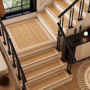 Puede incluir: Un juego de alfombrillas rectangulares tejidas en color tostado con un borde blanco, instaladas en una escalera de madera. Las alfombrillas presentan una textura de fibra natural y cubren cada escalón, incluyendo un tapete en el rellano.