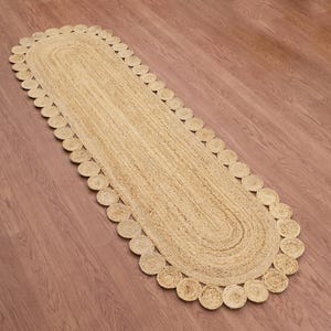 Pode incluir: Tapete corredor oval de juta com borda ondulada. O tapete é de cor bege natural e está colocado em um piso de madeira. O tapete é projetado para corredores ou entradas.