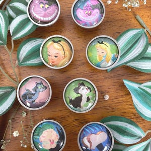 May include: Nine round, silver-toned cabinet knobs with colorful, vintage-style illustrations of characters from Alice in Wonderland. The characters include Alice, the Cheshire Cat, and the Mad Hatter.