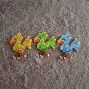 May include: Three small bead sprites, each depicting a different bird. The first is yellow with orange accents, the second is green with orange accents, and the third is blue with orange accents. All three sprites have brown legs and are standing on a brown surface.