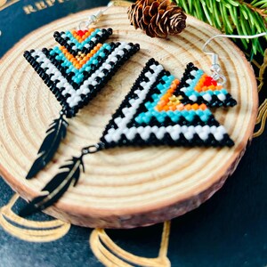 May include: A pair of beaded earrings with a geometric triangle design in black, white, turquoise, and orange. Each earring features a black feather dangle.