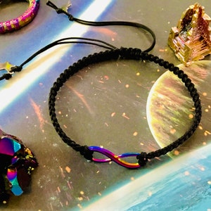Puede incluir: Un brazalete de cordón trenzado negro con un dije de infinito iridiscente.