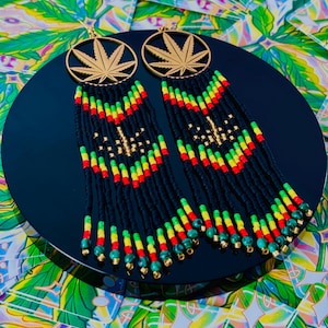 Peut inclure: Une paire de longues boucles d'oreilles en perles avec un pendentif en forme de feuille de marijuana dorée. Les perles sont noires, vertes, rouges et jaunes, et les boucles d'oreilles mesurent environ 10 cm de long.