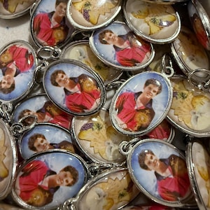 Könnte beinhalten: Eine Sammlung ovaler Anhänger mit silberfarbenen Metallrahmen. Jeder Anhänger zeigt ein Porträt einer Person in einem roten Hemd, und einige haben ein Design aus Trauben und Blumen. Die Anhänger sind wahrscheinlich für Halsketten.