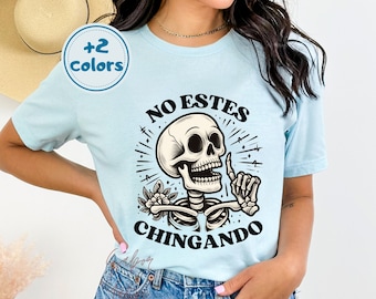 May include: A light blue t-shirt with a skull and crossbones graphic and the text "No Estes Chingando".