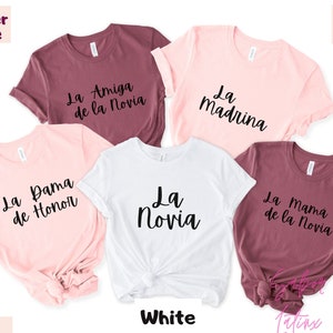 May include: Five t-shirts in different colors with Spanish text on them. The text on the shirts reads "La Amiga de la Novia", "La Dama de Honor", "La Novia", "La Madrina", and "La Mama de la Novia".