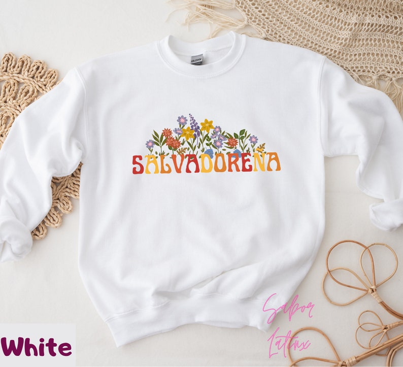 May include: White sweatshirt with a floral design and the text "SALVADORENA" in a retro font.