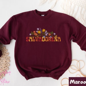 May include: Maroon sweatshirt with a floral design and the text "SALVADORENA" in a retro font.