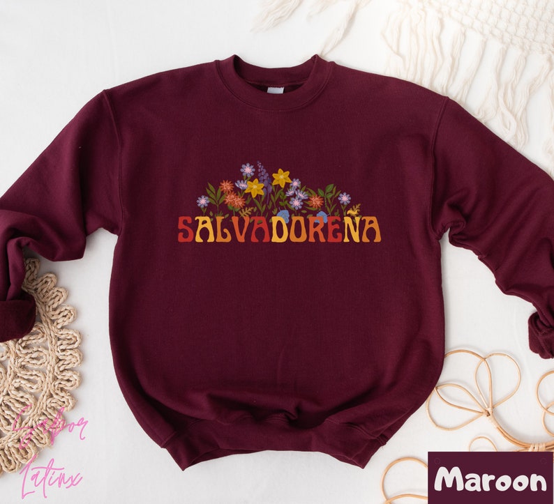May include: Maroon sweatshirt with a floral design and the text "SALVADORENA" in a retro font.