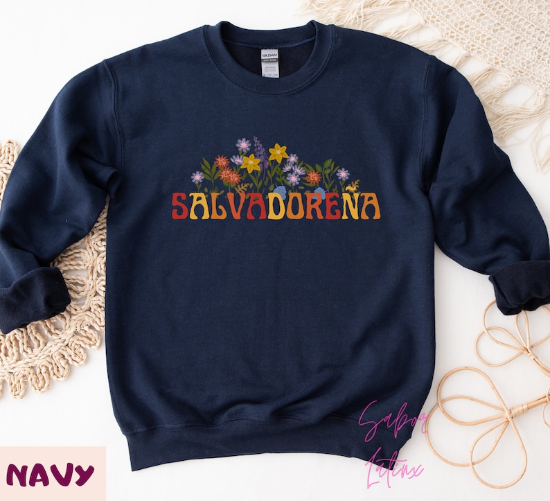 May include: Navy blue sweatshirt with a floral design and the text "SALVADORENA" in rainbow colors.
